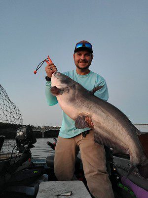 Photo of man on a small boat holding a large catfish