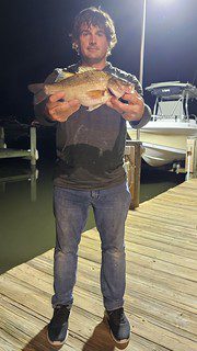 Photo of man holding a fish on a dock at night