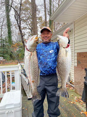 Photo of man outside a house holding up two large fish