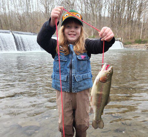 Photo of girl in a stream holding a trout