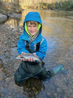 Photo of boy holding a fish in a stream