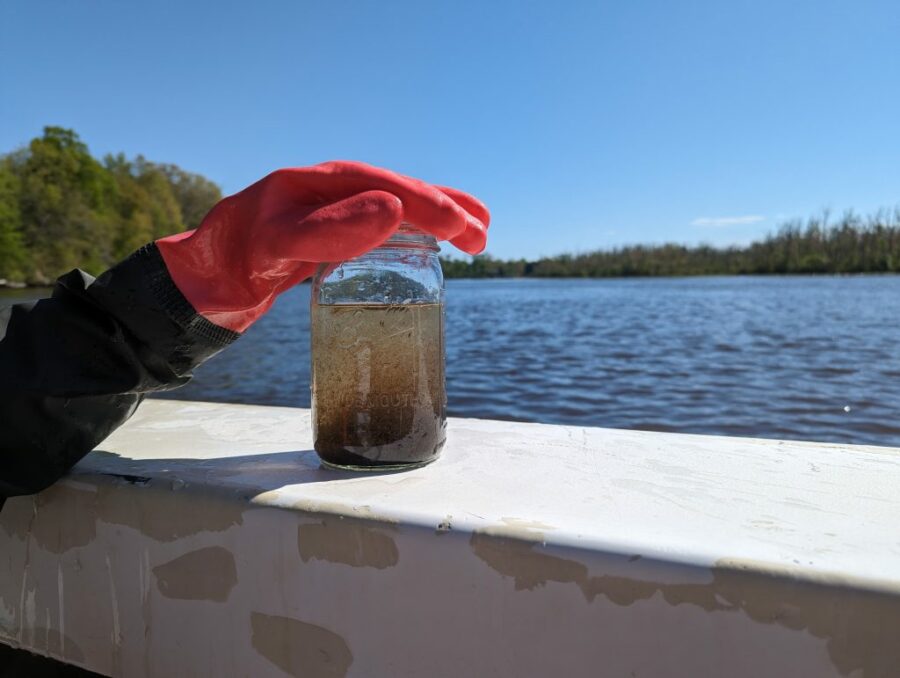 A biologist holds a jar full of murky water.